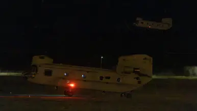 Twee Chinooks in het duister. Een in de lucht, de ander komt net los van het grasveld.
