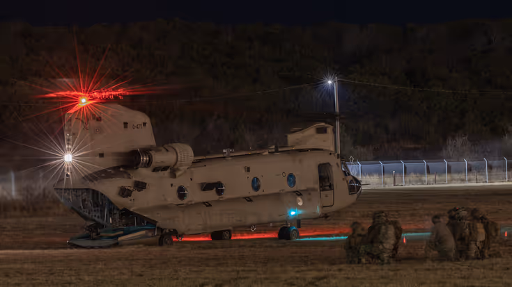 Nachtopname van een Chinook op de grond met luchtmobiele infanteristen er omheen.