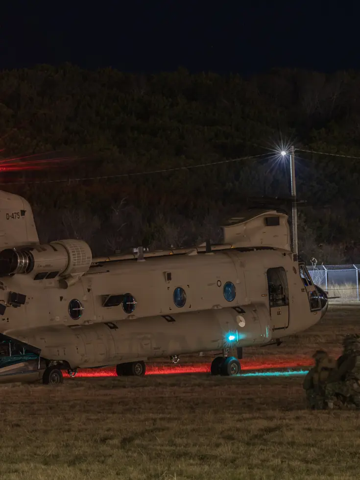Nachtopname van een Chinook op de grond met luchtmobiele infanteristen er omheen.