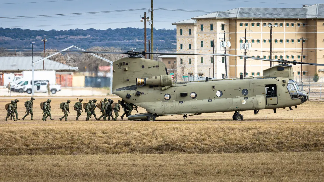 Militairen van 11 Luchtmobiele Brigade lopen via de laadklep een Chinook binnen op een veld van Fort Hood. Op de achtergrond gebouwen en heuvels.