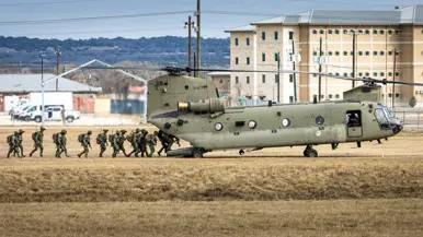 Militairen van 11 Luchtmobiele Brigade lopen via de laadklep een Chinook binnen op een veld van Fort Hood. Op de achtergrond gebouwen en heuvels.