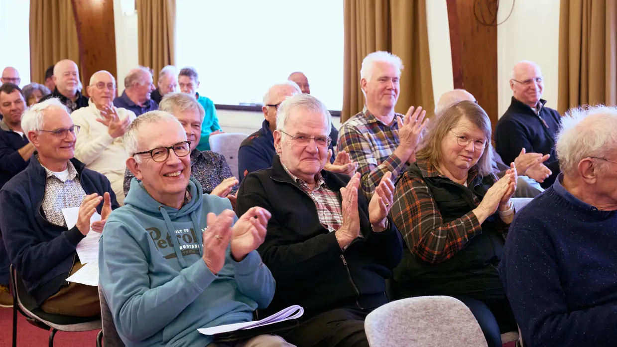 Heren en dames applaudiseren in een zaal.