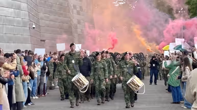 Militairen lopen door een haag van vrienden en familie en rode en oranje rookfakkels.
