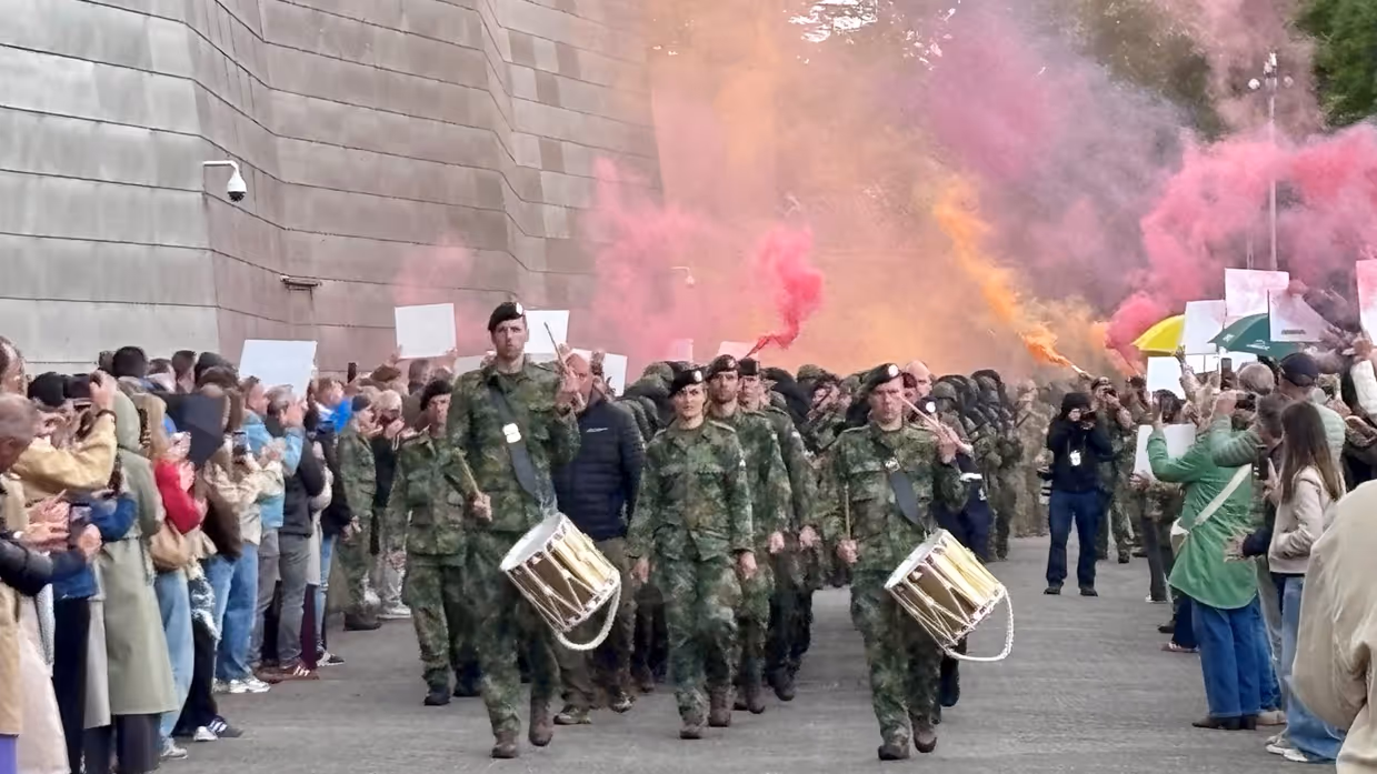 Militairen lopen door een haag van vrienden en familie en rode en oranje rookfakkels.