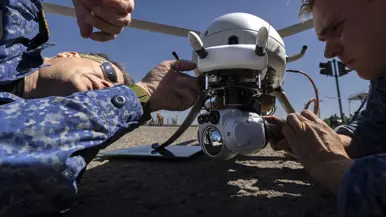 Twee mannen sleutelen aan een drone en liggen op de grond.