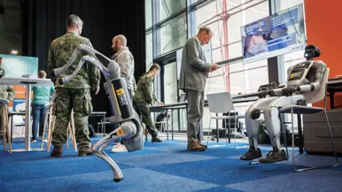 Een lopende en zittende robot met vier personen op de achtergrond.