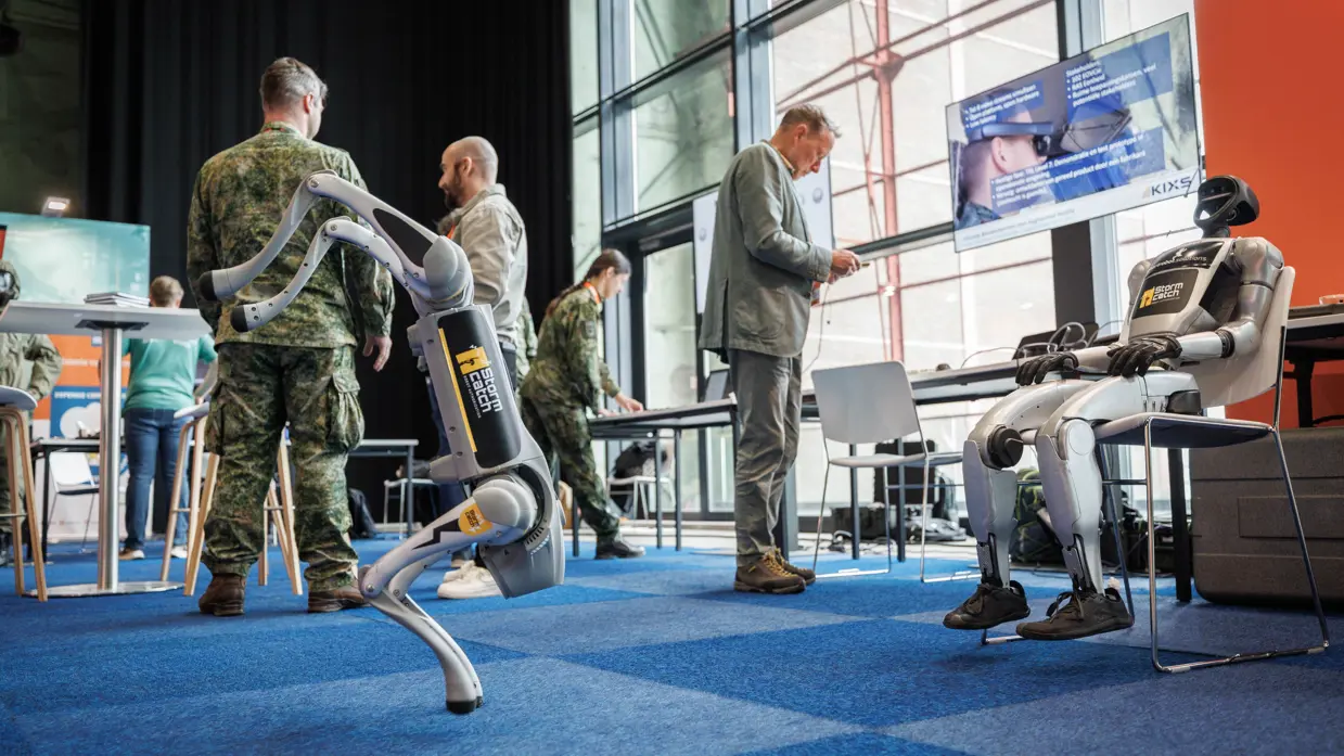 Een lopende en zittende robot met vier personen op de achtergrond.