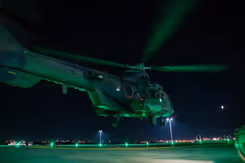 Groen aangelichte helikopter staat bijna aan de grond in het donker.