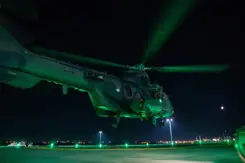 Groen aangelichte helikopter staat bijna aan de grond in het donker.