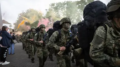 Militairen lopen door een haag van vrienden en familie en rode en oranje rookfakkels.