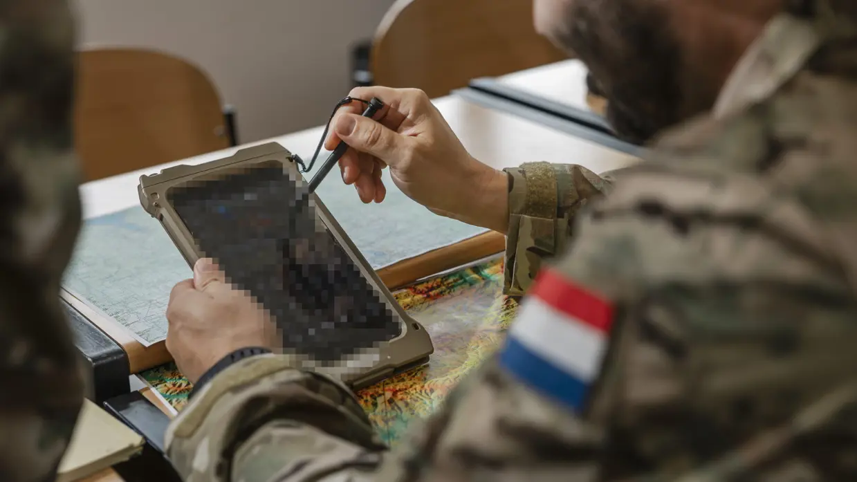 Een militair kijkt op iets wat lijkt op een grote mobiele telefoon.