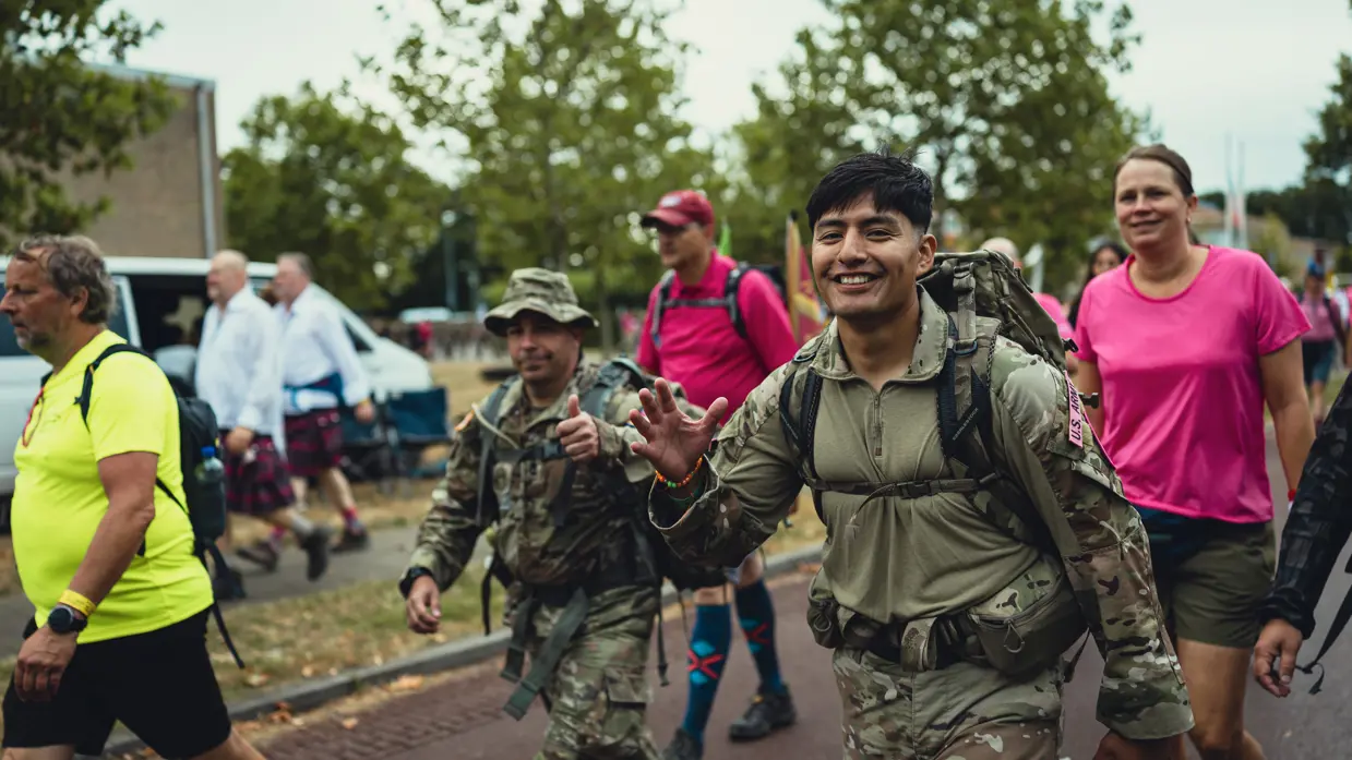  Een Amerikaanse militair zwaait en kijkt in de camera, omringd door andere lopers.