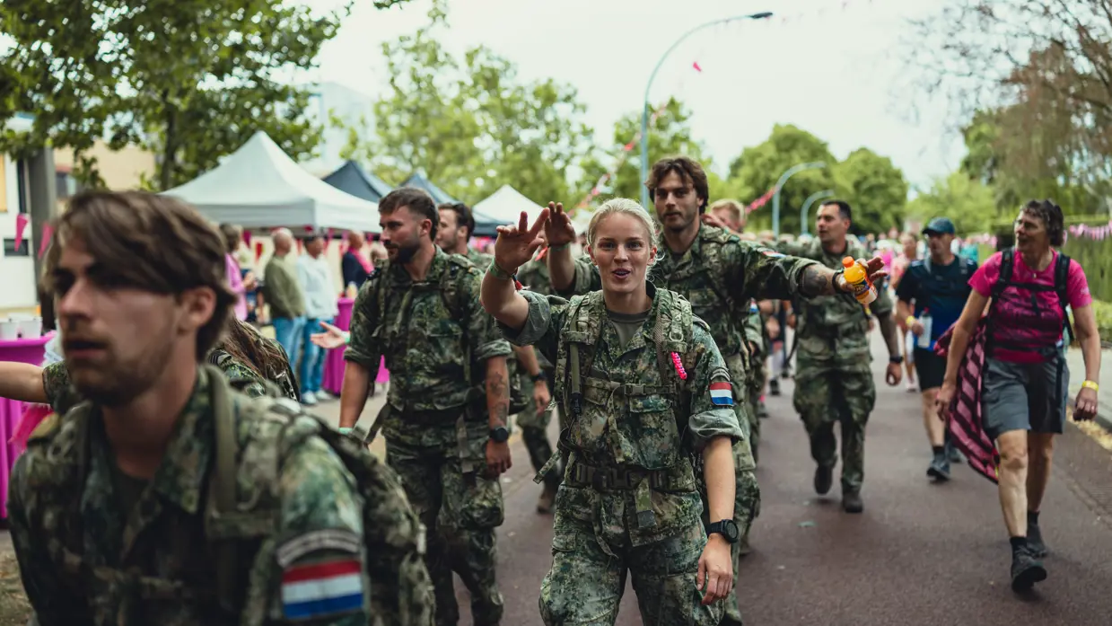  Een militaire groep loopt langs de fotograaf. Om hen heen dragen lopers roze shirts.&nbsp;
