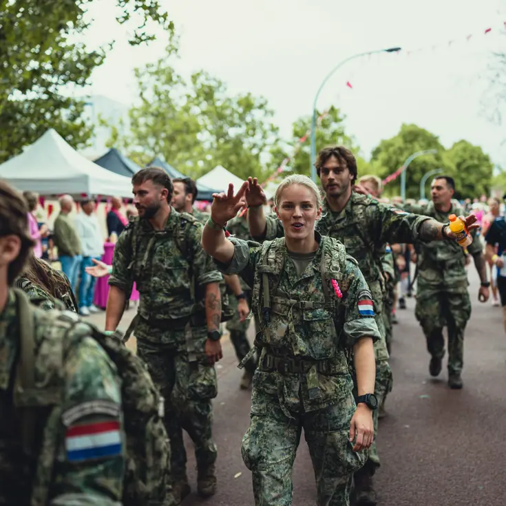  Een militaire groep loopt langs de fotograaf. Om hen heen dragen lopers roze shirts.&nbsp;