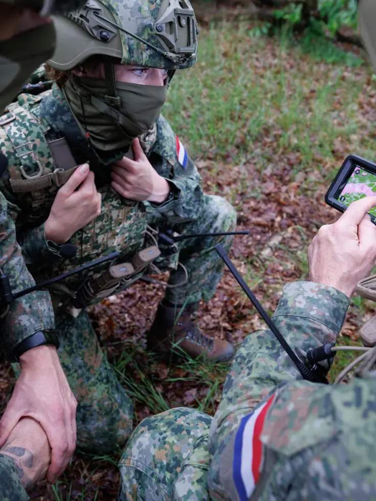 Militairen wijzen naar een kaartje op een telefoonscherm.