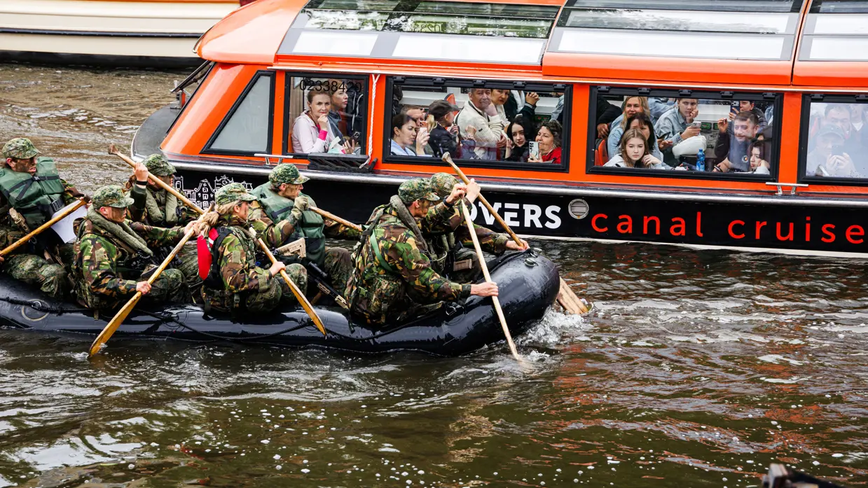 De deelnemers aan de NWT roeien in rubberboten door Amsterdam.