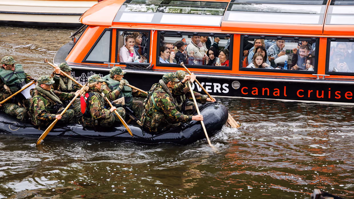 De deelnemers aan de NWT roeien in rubberboten door Amsterdam.