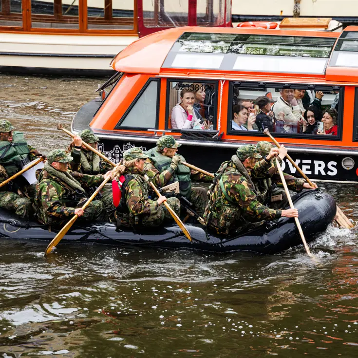 De deelnemers aan de NWT roeien in rubberboten door Amsterdam.