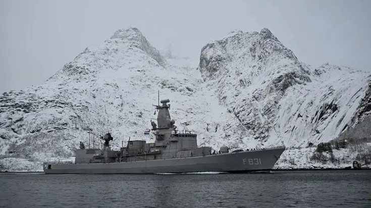 De Zr.Ms. Van Amstel vaart voor besneeuwde rotsen langs.