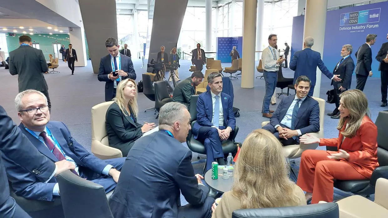 Groepje mensen zit op stoelen in een kring tijdens overleg in conferentieruimte.