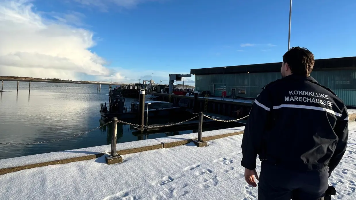 Marechaussee kijkt uit over besneeuwde haven.