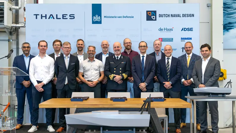 Heren in een net pak en een in uniform poseren voor een bord met bedrijfsnamen.