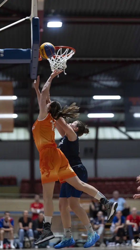Een basketballer onder de basket in een sportzaal.