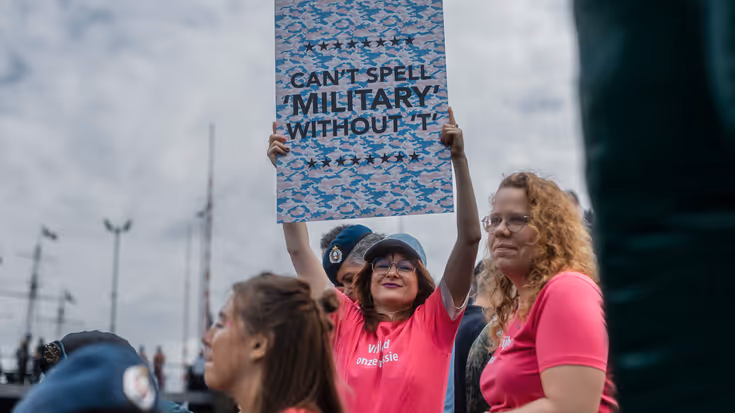 Een vrouw houdt een bord omhoog waarop staat: Can't spell 'military' without 'T'. 