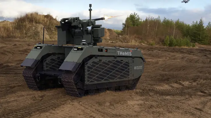 Een onbemand militair rupsvoertuig genaamd THEMIS met een kanon schiet op een zanderig terrein, terwijl een drone boven vliegt in een open landschap. 