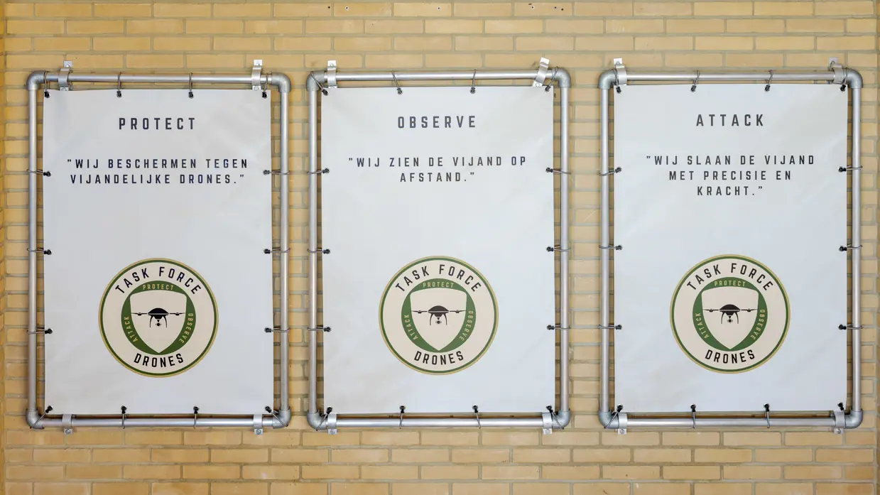 Logo Task Force Drones wordt onthuld en borden met protect, observe en attack; hun motto.