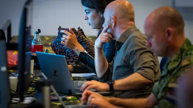 Een vrouw in overleg met een mannelijke collega, terwijl de twee naar hun beeldschermen kijken.