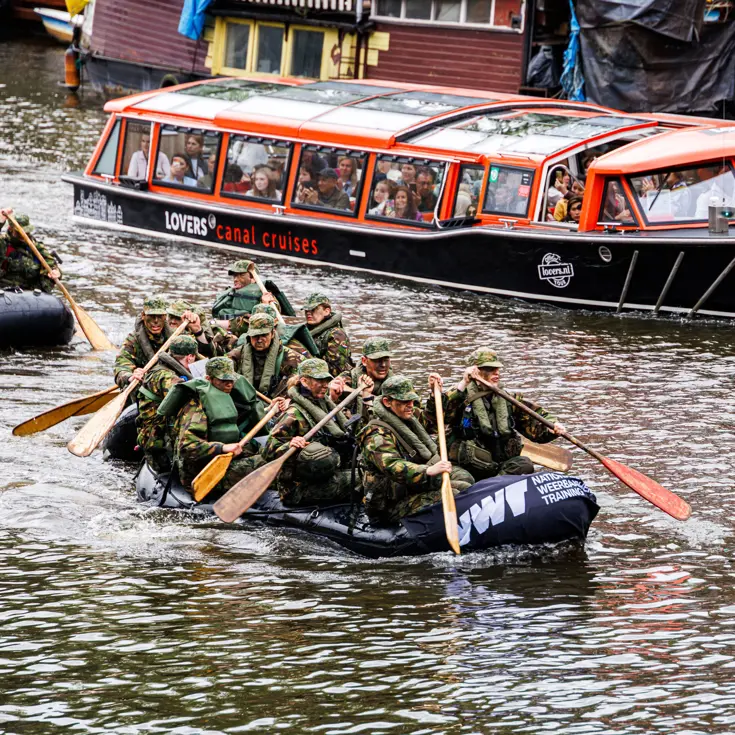 De deelnemers aan de NWT roeien in rubberboten door Amsterdam.