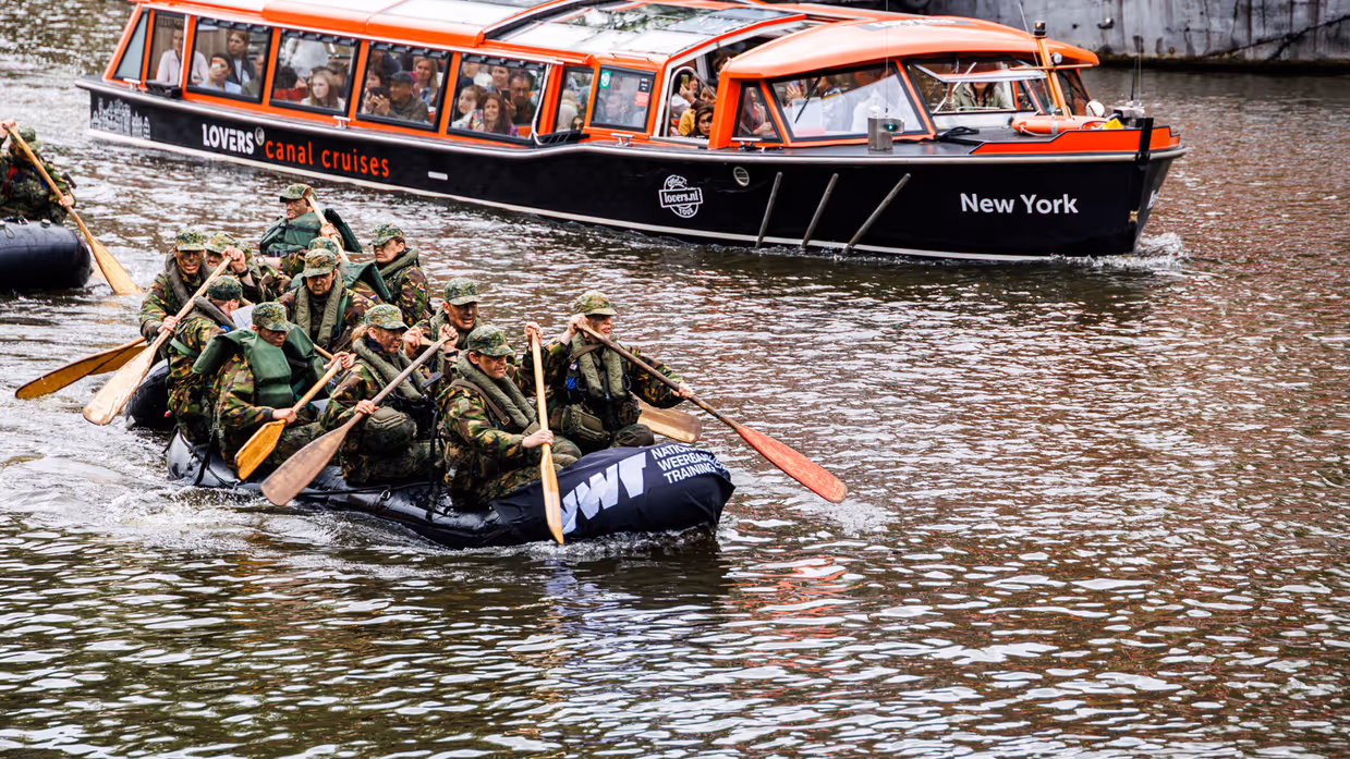 De deelnemers aan de NWT roeien in rubberboten door Amsterdam.