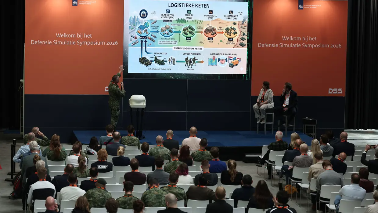 Een militair op een podium geeft een presentatie.