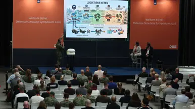 Een militair op een podium geeft een presentatie.