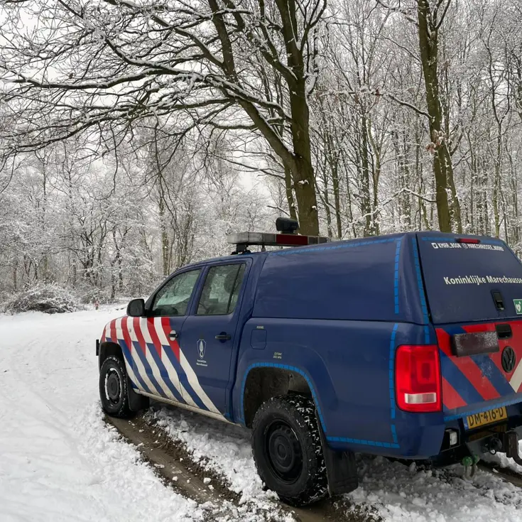 Voertuig van de Marechaussee in een besneeuwd bos.