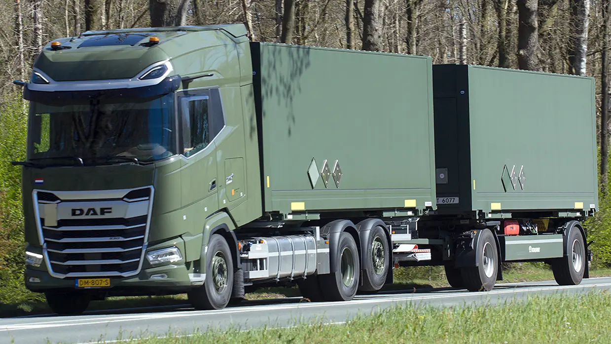 Een groene DAF vrachtwagen met twee aanhangers rijdt over een weg, omringd door bomen en gras.