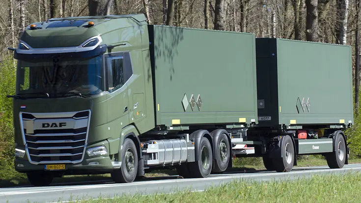 Een groene DAF vrachtwagen met twee aanhangers rijdt over een weg, omringd door bomen en gras.