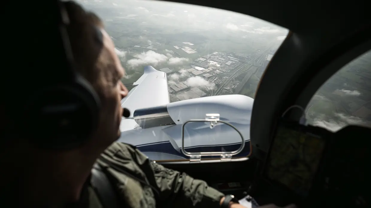  Vlieger van de Koninklijke Marechaussee kijkt tijdens een vlucht vanuit de cockpit over een industriegebied.