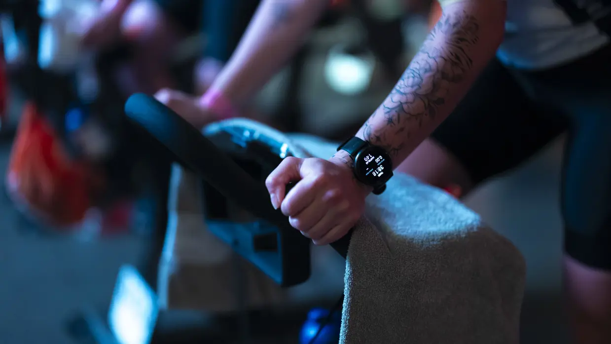 Close up van sporthorloge en handen op het stuur van een indoorbike.