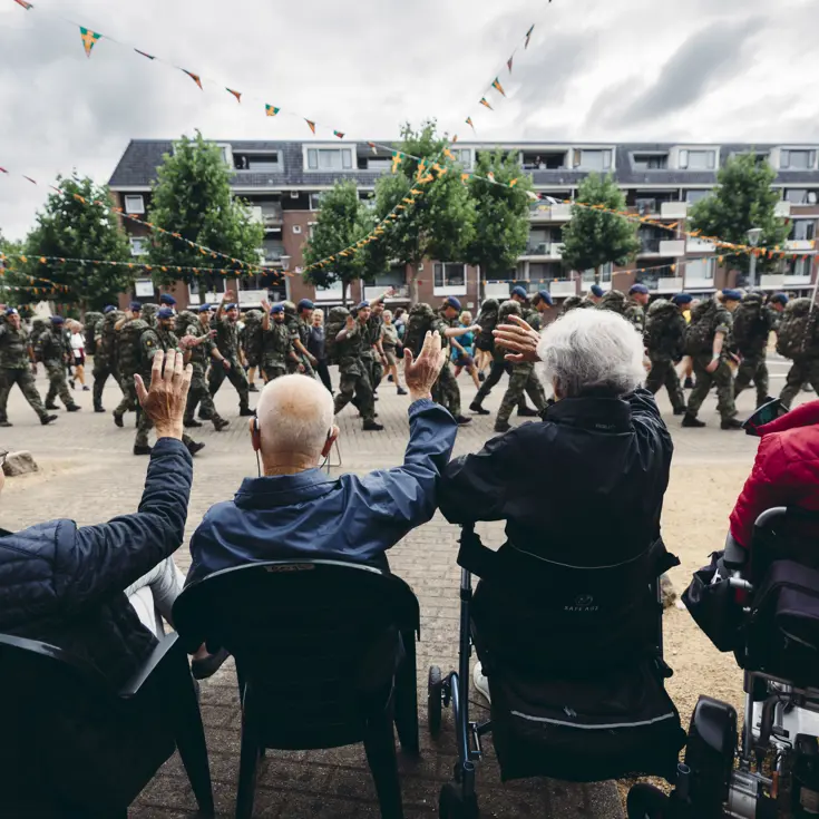 Een groepje oudere toeschouwers, op de rug gezien, moedigt een detachement van de Marechaussee aan tijdens de Nijmeegse 4Daagse. 