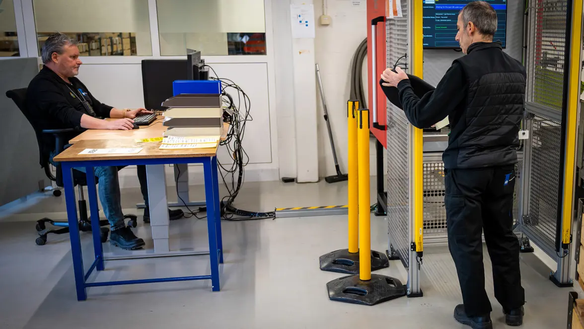 Twee man bezig met het keuren van ballistische platen. Één achter een computerscherm en één bij de scanner.