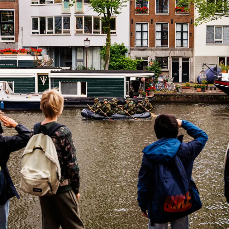 De deelnemers aan de NWT roeien in rubberboten door Amsterdam.