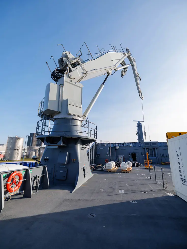 Een grijze kraan op het dek van het schip, een donkergrijze reddingsboot en het predicaat met daarop ‘Den Helder’.