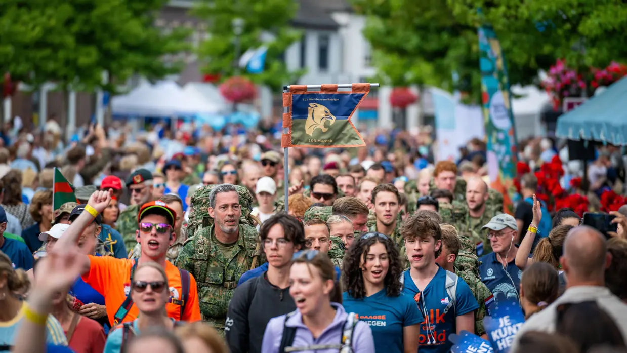 Een groep mensen aan de wandel tijdens de 4Daagse, in het midden een club militairen van 103 Marechaussee Eskadron.