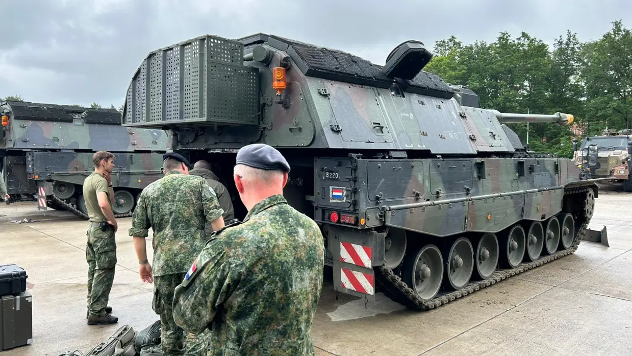 Vier personen in militaire kledij inspecteren een militair voertuig.