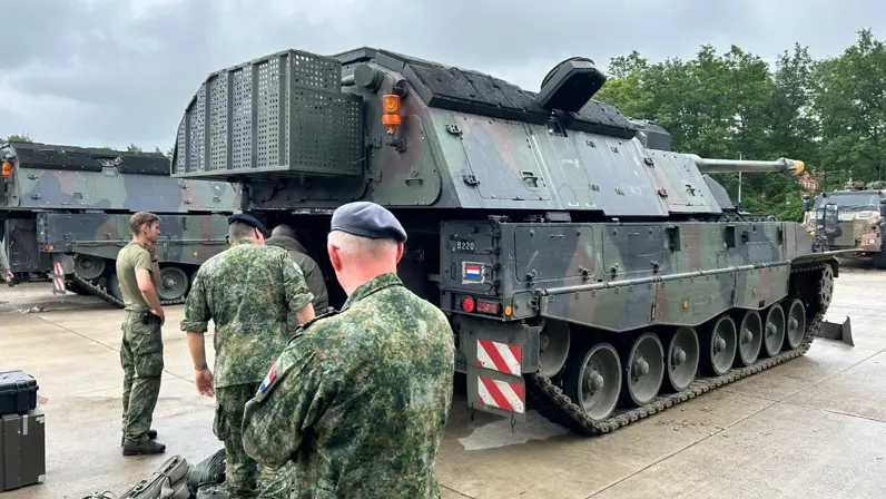 Vier personen in militaire kledij inspecteren een militair voertuig.