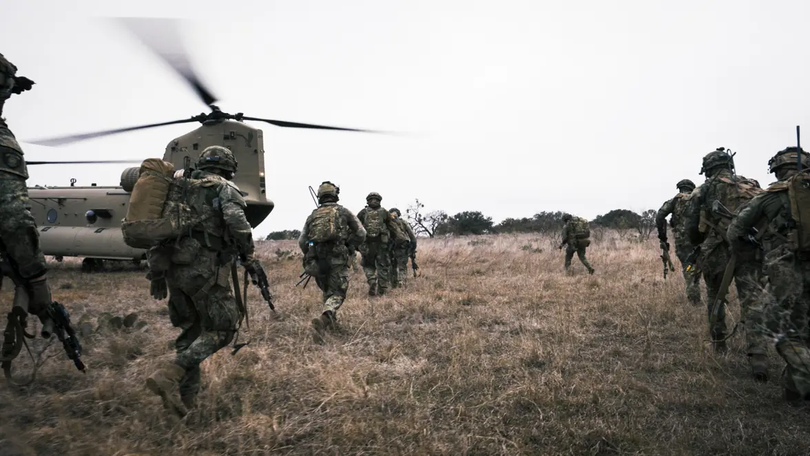 In het veld lopen landmachtmilitairen naar de openstaande achterklep van een Chinook met draaiende rotorbladen.