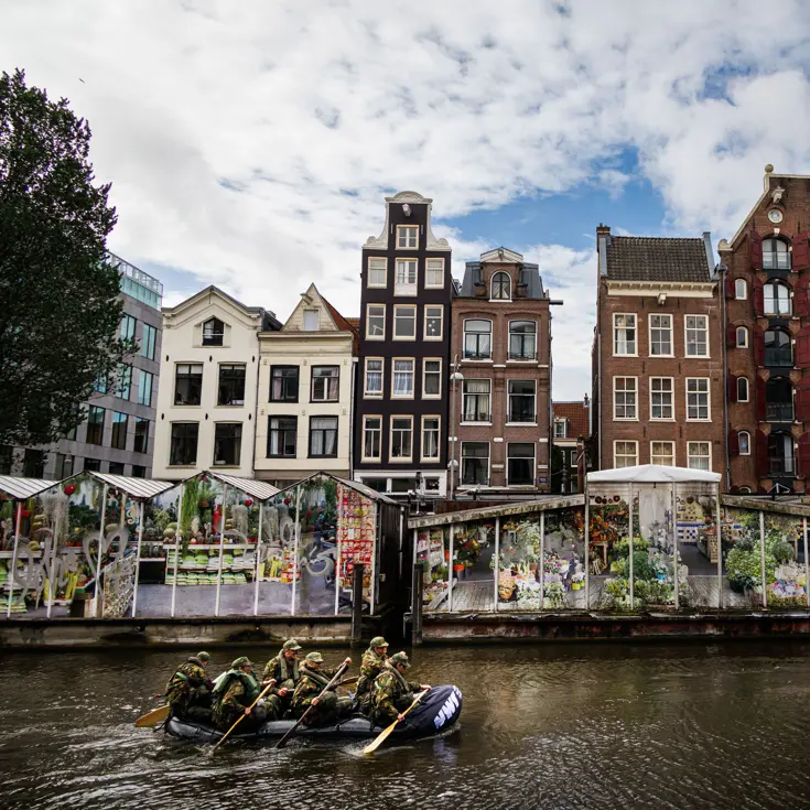 De deelnemers aan de NWT roeien in rubberboten door Amsterdam.