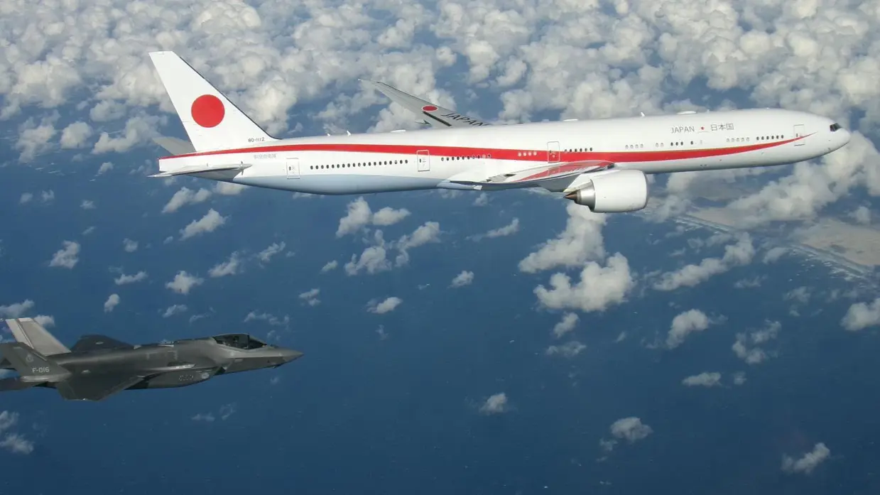Een groot wit vliegtuig met een rode glooiende lijn over de romp en de tekst ‘Japan’, en een grote rode stip op de staart vliegt naast een Nederlandse F-35.